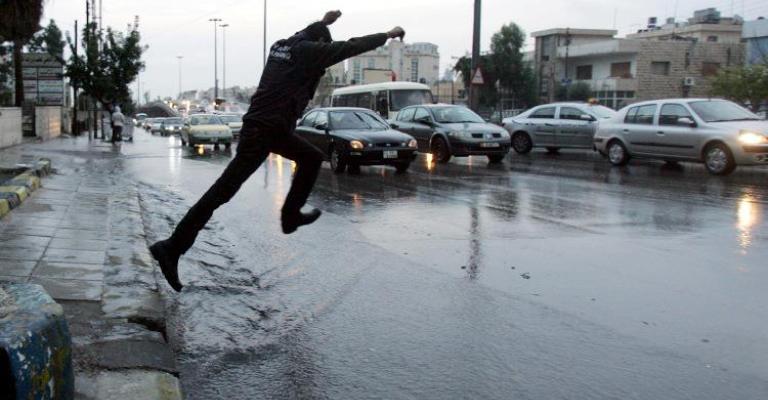 مواطن يحاول عبور الطريق الذي فاض بمياه الأمطار، عدسة حمزة مزرعاوي/ فيسبوك