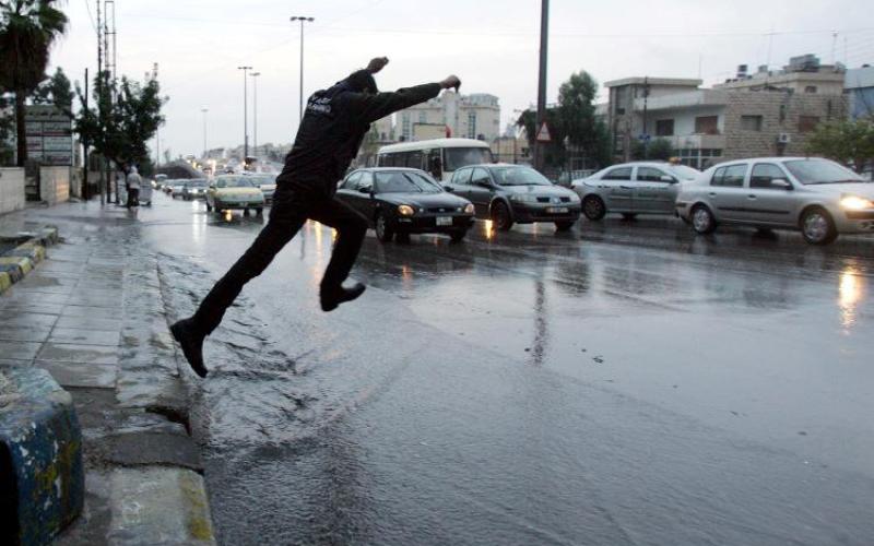 مواطن يحاول عبور الطريق الذي فاض بمياه الأمطار، عدسة حمزة مزرعاوي/ فيسبوك